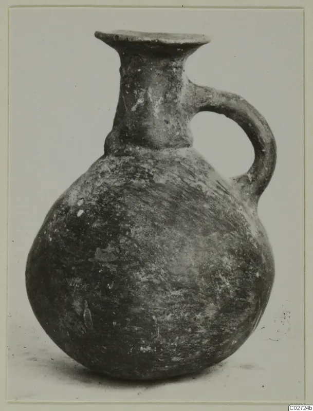 Round-bodied jug with a flared mouth and a single loop handle, dark burnished surface, against a plain background.