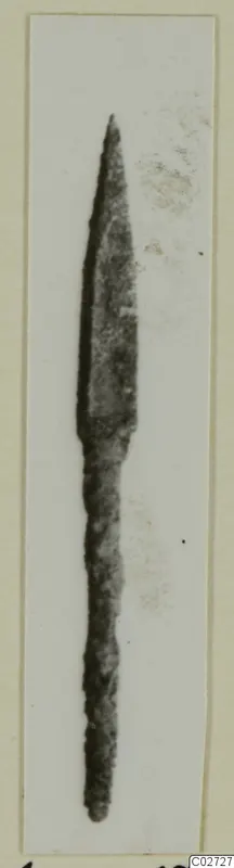 Bronze arrowhead, long and narrow with a pointed tip and slender shank, photographed on a pale card mount