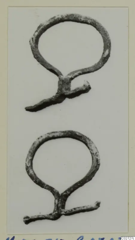 Two bronze loop-shaped fragments with short projecting arms, photographed on a pale background.