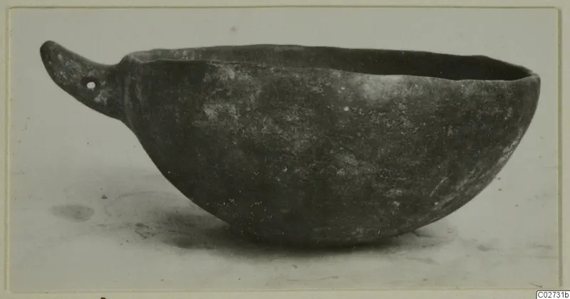Red Polished IV bowl with a pierced flat handle, shown in side view on a pale surface