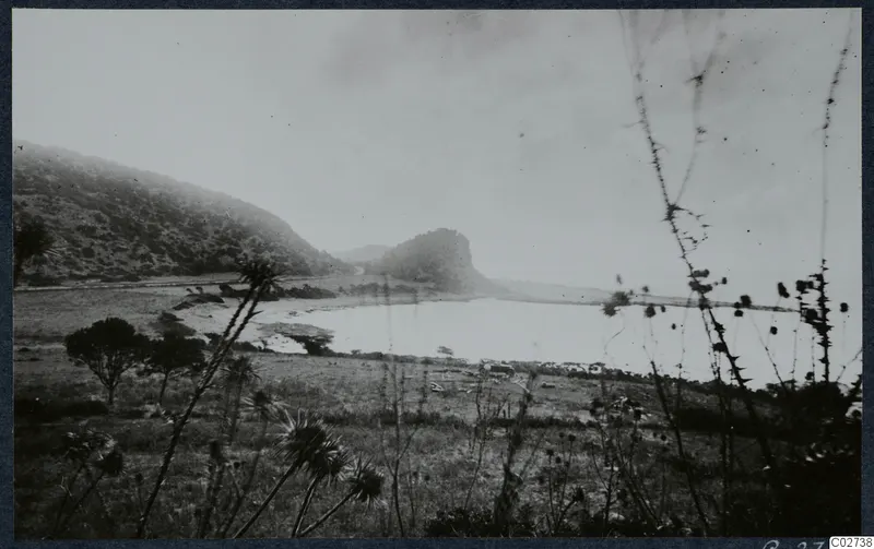 Landscape at Vouni with a scrub-covered hillside, a rocky knoll and a pale stretch of water in the middle distance
