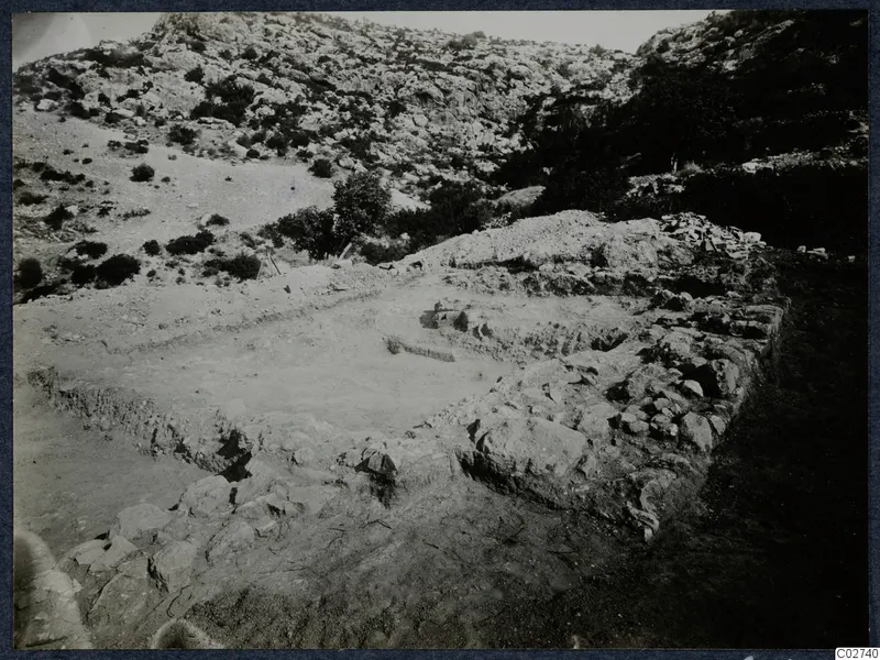 Excavated stone foundations of the Paradisiotissa temple at Vouni, seen from the north-west, with a rocky hillside behind.