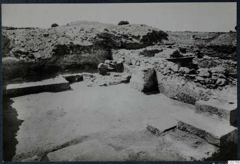 Excavated area at Soli with stone walls, large flat slabs and earth banks rising behind
