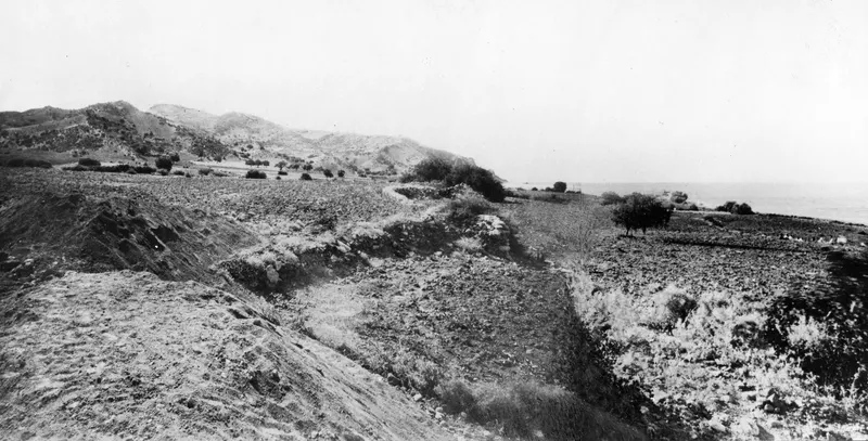 View towards Vouni from the excavation at Mersinaki, with low walls, rocky hills and the sea beyond.