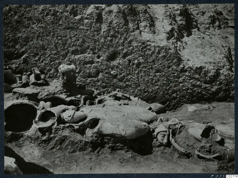 Statue fragments lying together in an excavation at Mersinaki, with a carved face and heads visible among broken bodies.