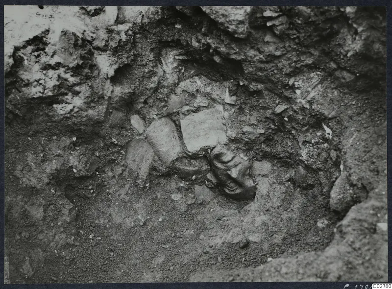 Carved stone head in situ in H 15 at Mersinaki, half-buried in soil among stones
