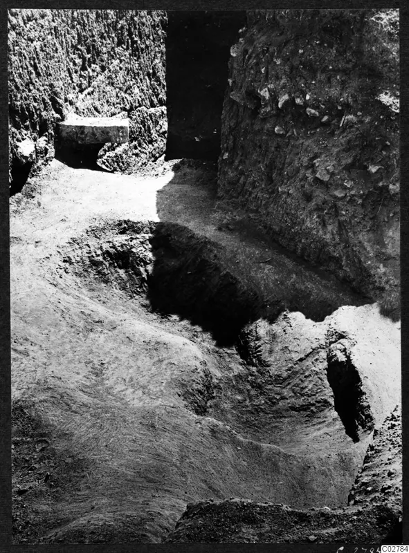 Excavated pit at Mersinaki with steep earth walls and a flat stone slab set into the upper left wall