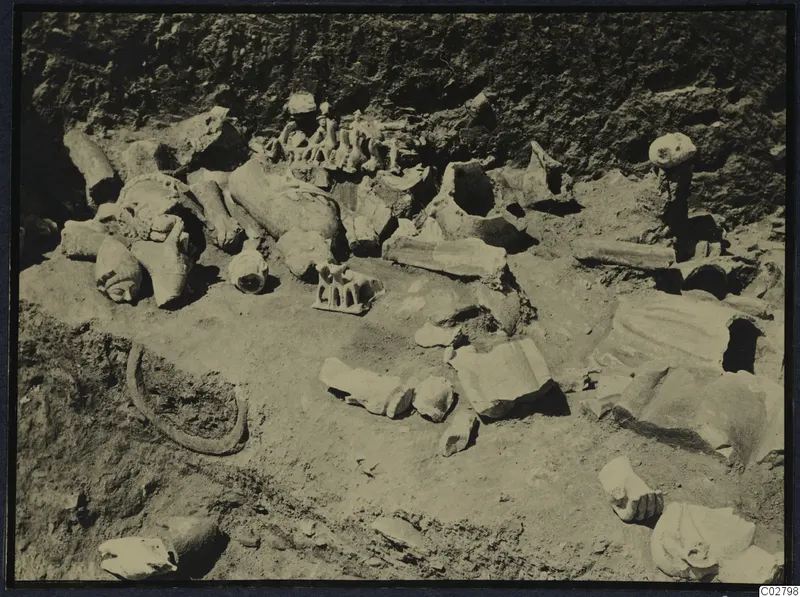Broken stone sculpture fragments lying in excavated soil at Mersinaki, including several heads, a hand and body pieces