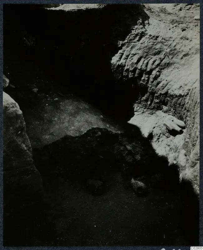 Objects lying in situ in an excavated pit at Mersinaki, with pale soil walls and dark shadow across the floor.