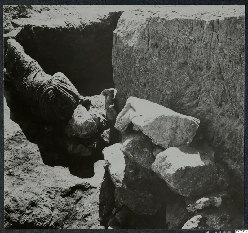 Excavation pit at Mersinaki with large pale stone blocks and a rolled dark bundle among the finds in situ