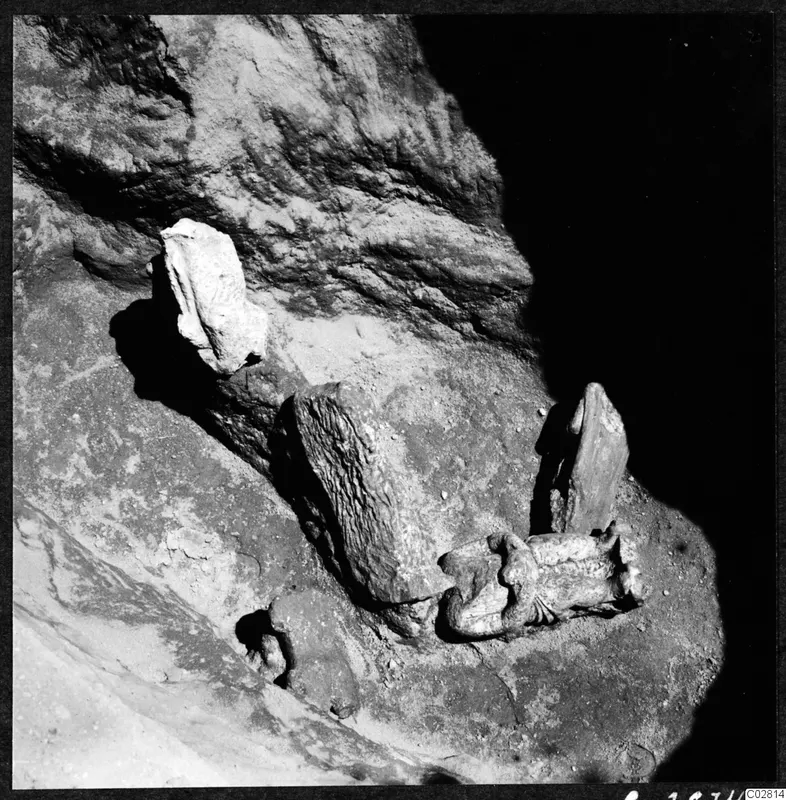 Broken stone sculpture fragments lying in situ against a rock face at Mersinaki