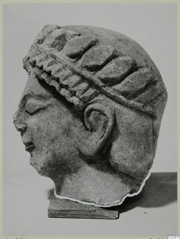 Limestone sculpture of a female head in profile, wearing a leafy wreath or band, with the base cut away at the neck.