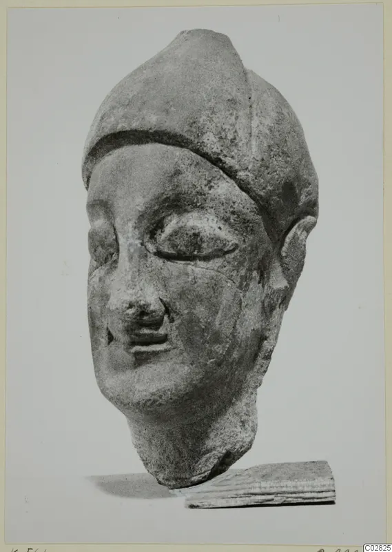 Limestone head with a tall, rounded headdress and almond-shaped eyes, shown in three-quarter view resting on a wooden block