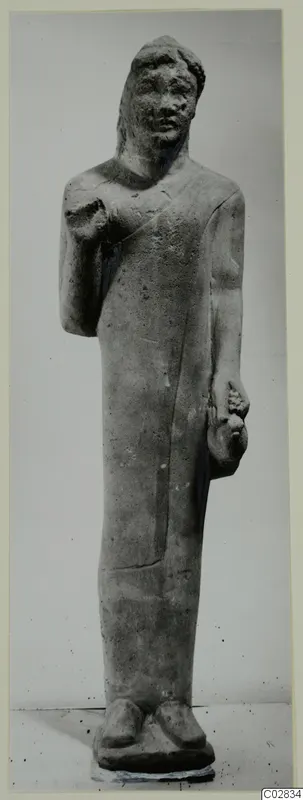 Limestone statue of a standing figure from Kition, arms bent at the chest and hip, shown against a plain grey background.