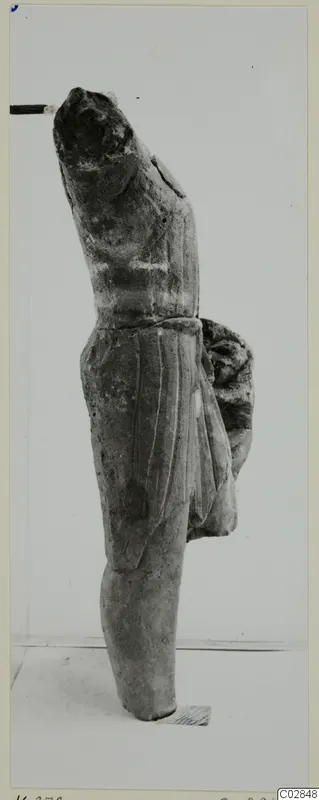 Limestone statue fragment of a standing figure in a draped garment, shown in side view
