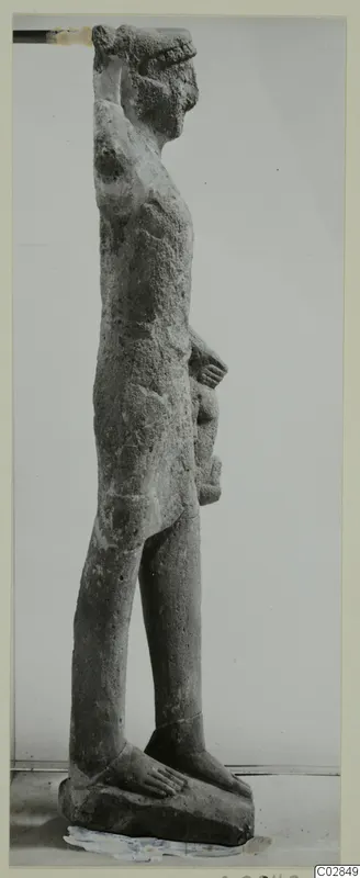 Side view of a standing limestone statue with one arm raised to the top of the head, on a rectangular base