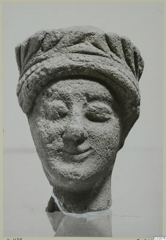 Limestone head of a figure wearing a grooved headdress, with downcast eyes and a slight smile