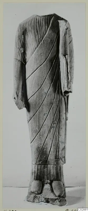Limestone statue of a standing headless figure in a draped garment with diagonal folds