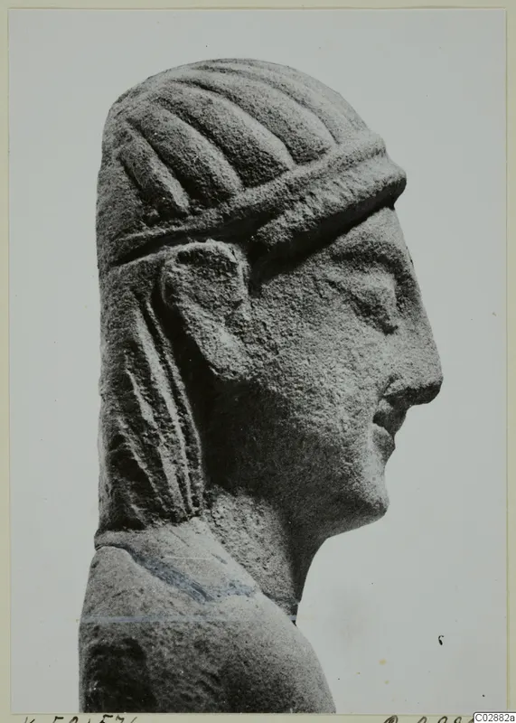 Carved limestone head in right profile, with grooved hair, a raised band across the forehead and long locks falling behind the ear.