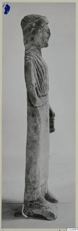 Limestone statue of a standing figure in profile, wearing a long draped garment