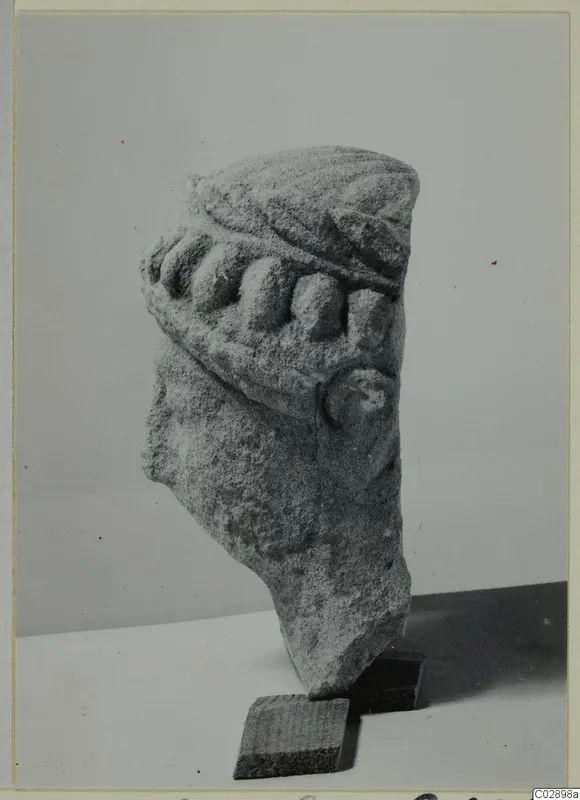 Broken limestone statue head with a row of rounded forms across the brow, photographed on wooden blocks