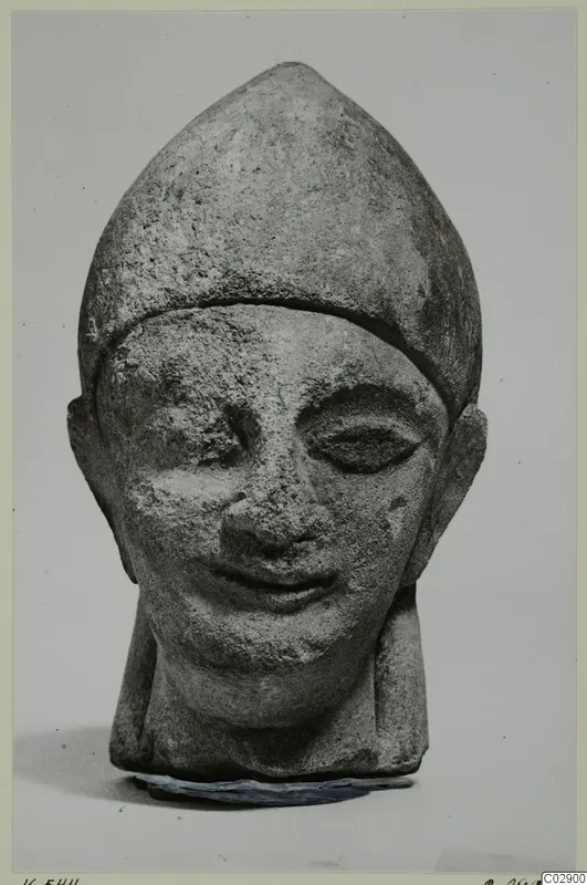 Limestone head of a figure wearing a tall pointed cap, from Kition, photographed against a plain grey background
