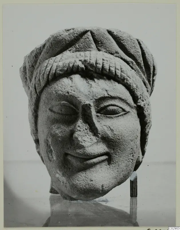 Carved limestone head with a wrapped headdress and slight smile, seen from the front