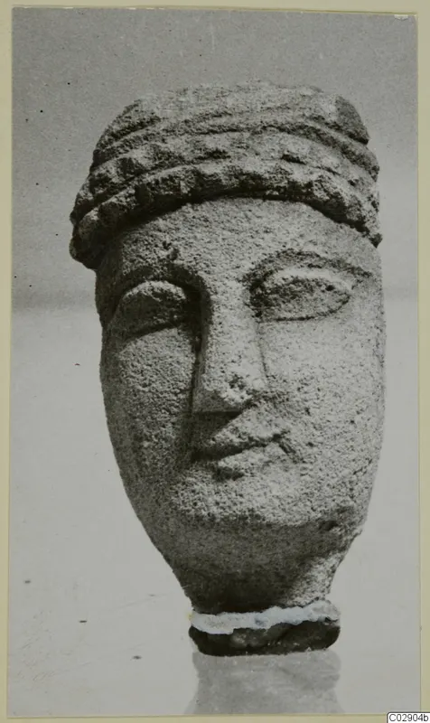 Limestone head of a figurine with a banded headdress and carved face, photographed against a plain grey background
