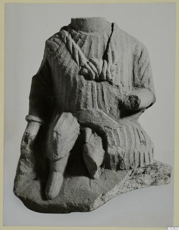 Limestone seated figure, headless, with draped garment and bent arm, shown against a plain grey background