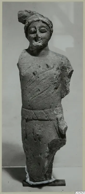 Limestone statue of a standing figure with a cap-like headdress, a belt and an arm broken off, from Kition.