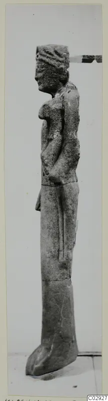 Limestone statue of a standing figure, seen in side view, with arms folded across the chest.
