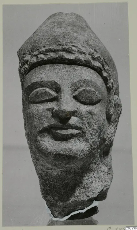Limestone head with a band-decorated headdress and downcast eyes, from Kition, photographed frontally against a grey background.