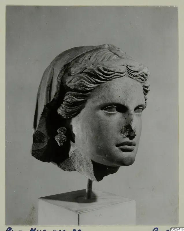 Marble head of a woman with wavy hair swept back under a veil, shown on a square stand.