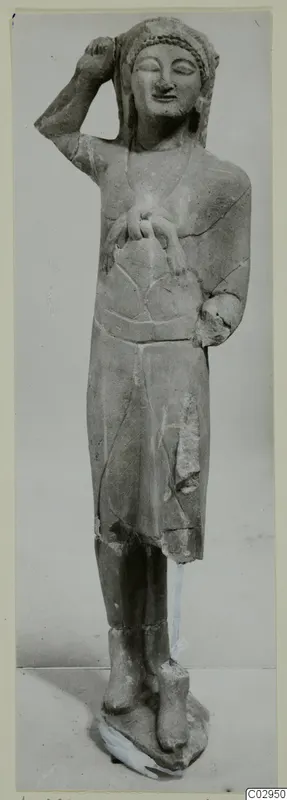 Limestone statue from Kition of a standing figure with one hand raised to the head and the other at the chest.