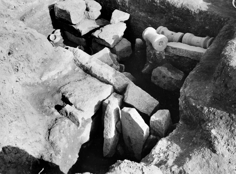 Excavation of Tomb 16 at Amathus: cut stone blocks in a trench, with two cylindrical stone pieces on a ledge at right