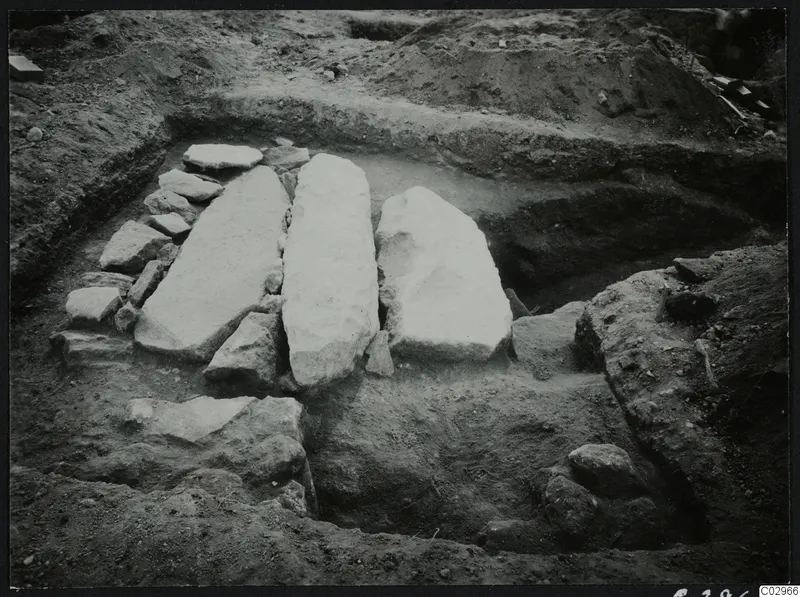Excavation at Amathus with three large pale stone slabs standing in a trench, surrounded by smaller stones.