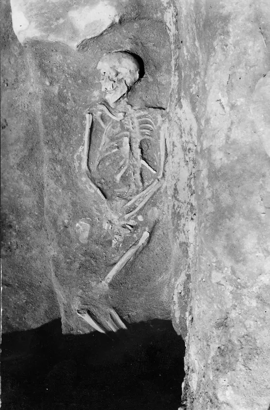 Skeleton lying in Tomb 16 at Amathus, with the skull, ribcage and arm bones visible against the tomb wall.