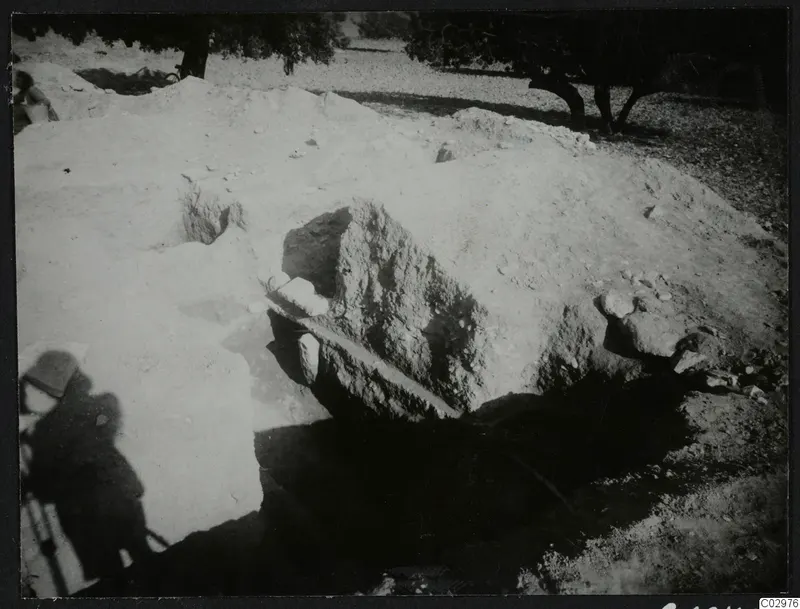 Excavation at Amathus with stones and trees; pale spoil heaps around a dark opening and a large block
