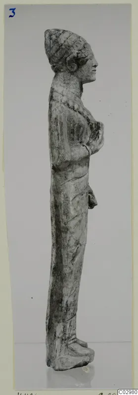 Limestone statuette of a standing female figure in profile, from Vouni, with arms folded across the chest.