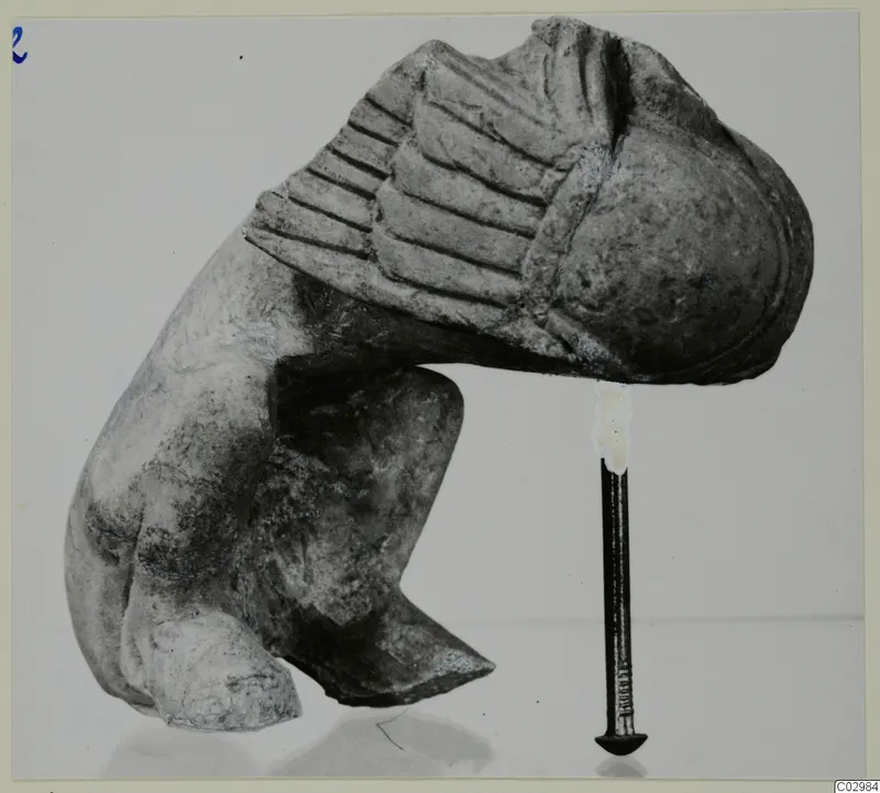 Limestone sculpture fragment from Vouni with a ribbed upper section, photographed beside an iron nail