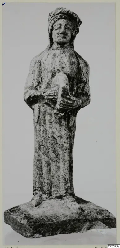 Limestone figurine from Vouni of a standing robed figure with a head covering, holding a small object at the chest