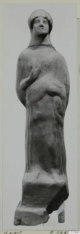 Terracotta figurine of a standing draped figure with a close-fitting head covering and one arm bent across the chest.