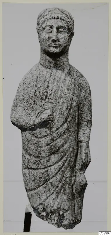 Limestone statue from Vouni of a standing figure in a draped cloak, one arm bent across the chest.