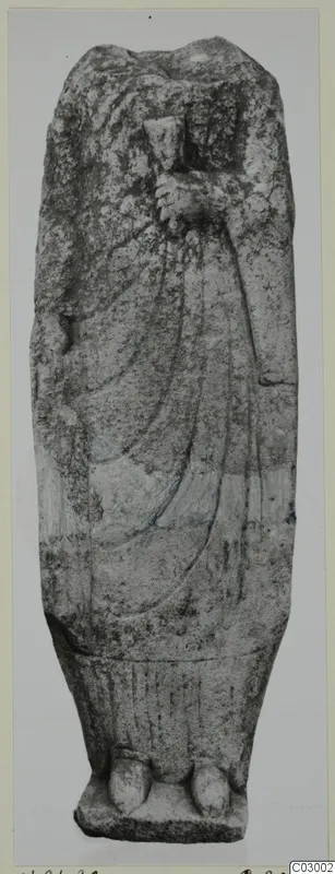 Limestone statue from Vouni of a standing draped figure with a broken head, one hand raised to the chest.