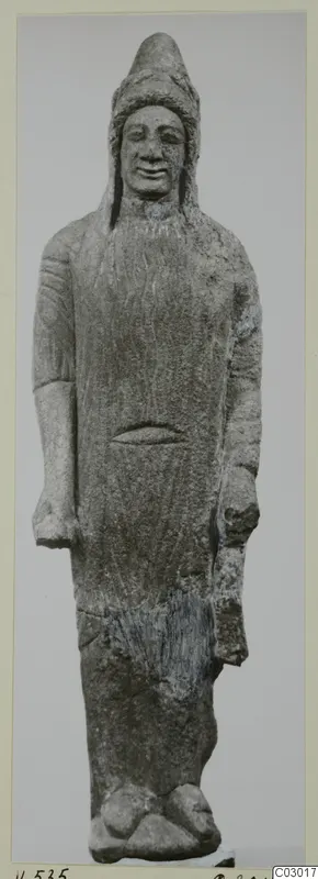 Limestone statue of a standing figure in a long garment and tall cap, photographed against a grey backdrop.