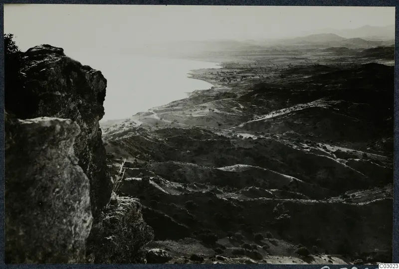 View from a rocky outcrop over a bay and rolling hills near Vouni, with scattered trees and a track winding across the slopes