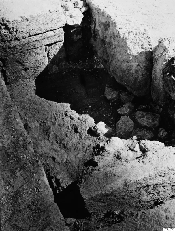 Excavation trench at the palace at Vouni, with large cut stone blocks and loose stones in a dark hollow