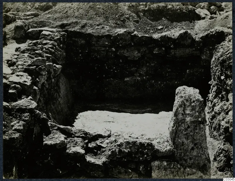 Excavated stone-walled pit at Vouni Palace with a standing stone block on the right and a pale floor surface.