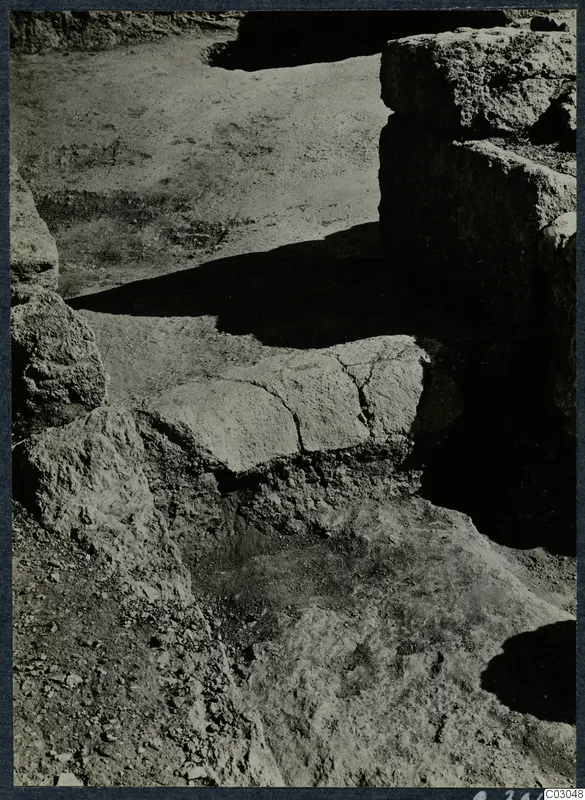 Excavated area at Vouni palace with rough stone blocks, a cracked flat slab, and a standing wall in shadow
