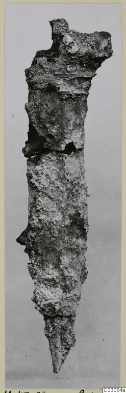 Corroded iron dagger blade, photographed upright against a grey backdrop.